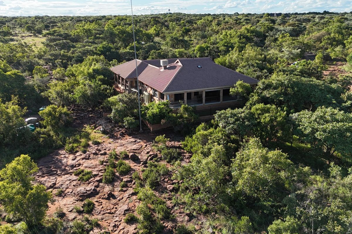 Aerial view of a residential property nestled in a natural, wooded landscape with a tiled roof and wrap-around covered patio.