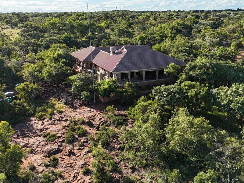 Aerial view of a residential property nestled in a natural, wooded landscape with a tiled roof and wrap-around covered patio.
