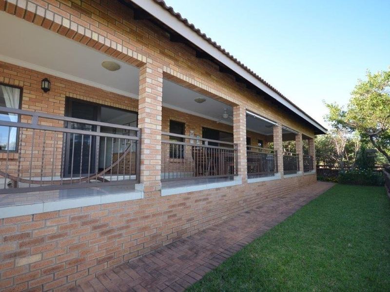 A spacious covered brick patio featuring a metal balustrade, overlooking a well-maintained garden and paved walkway.