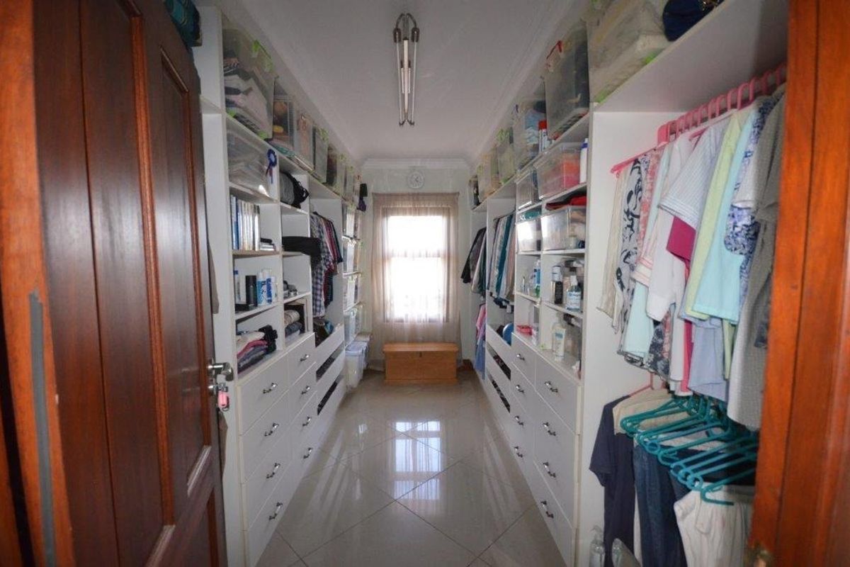 A walk-in closet featuring extensive built-in cabinetry with drawers and shelving, tiled flooring, and a window providing natural light.