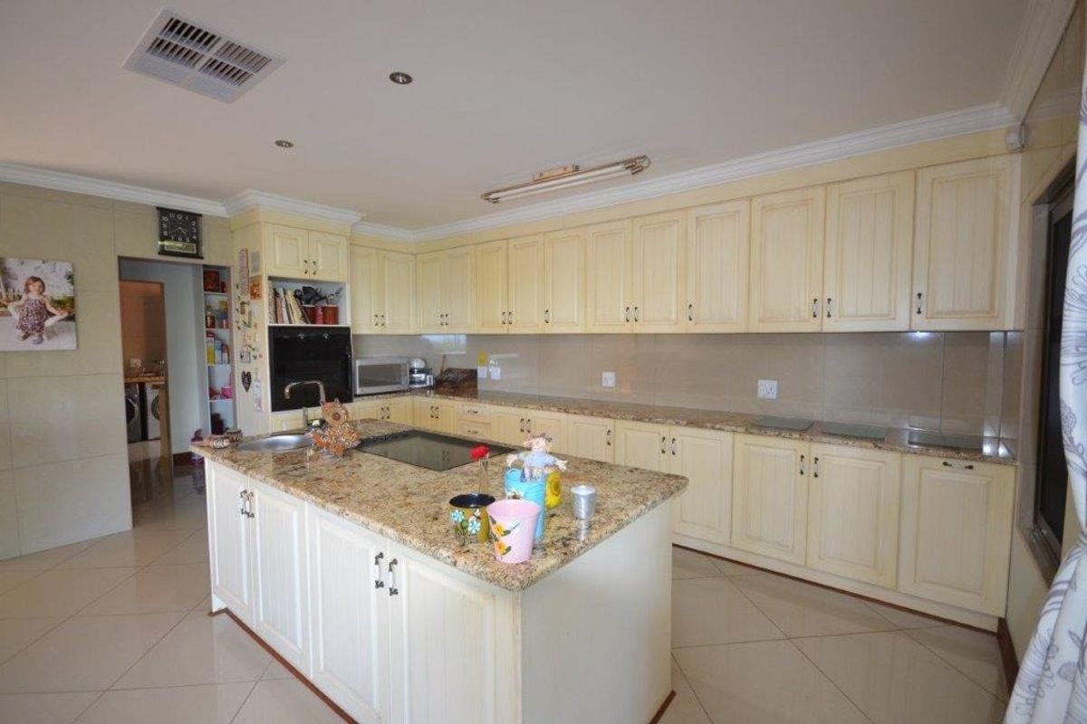 Spacious kitchen featuring granite countertops, a central island, built-in oven, and ample cabinetry, offering a functional layout with tiled flooring throughout.