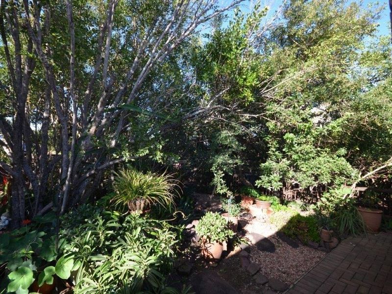 A lush, established garden area featuring mature trees, dense foliage, and brick paved pathways, providing a private and shaded outdoor setting.