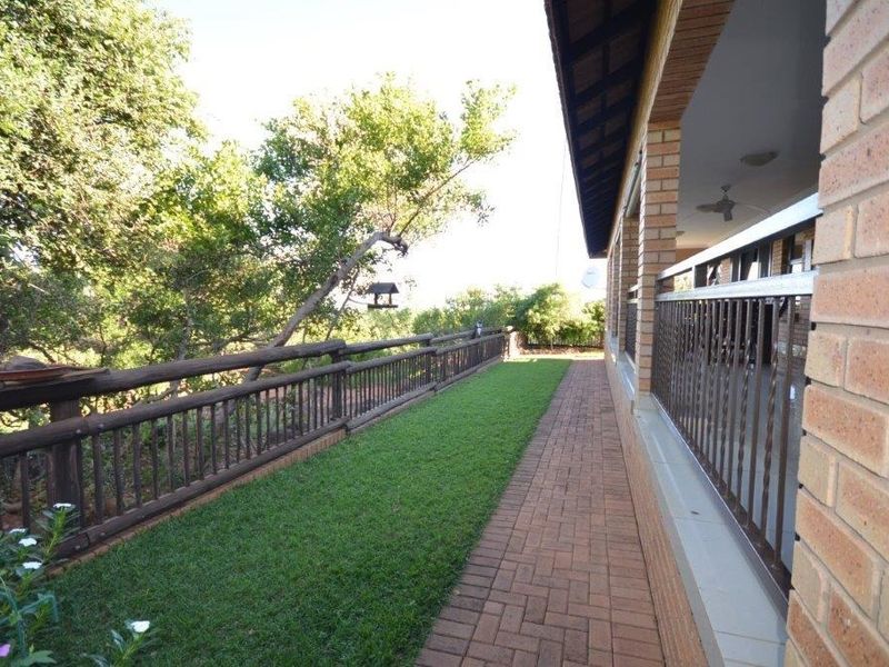 A covered patio area featuring brick paving, brick pillars, and a metal balustrade overlooking a garden space.