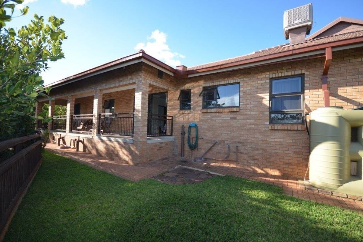 Rear view of the property featuring a brick facade, a covered patio area, and a large water tank set within a landscaped garden.