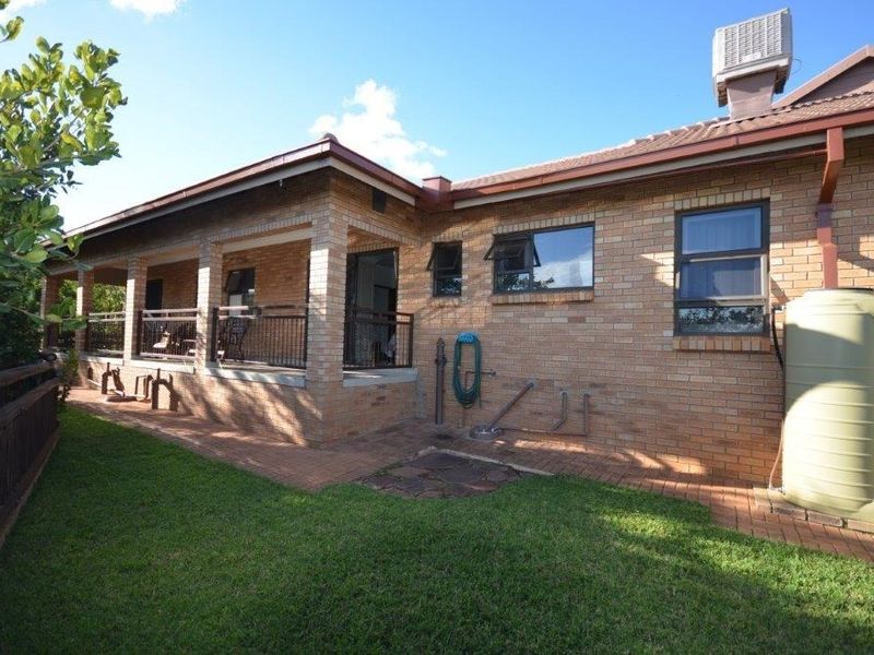 Rear view of the property featuring a brick facade, a covered patio area, and a large water tank set within a landscaped garden.