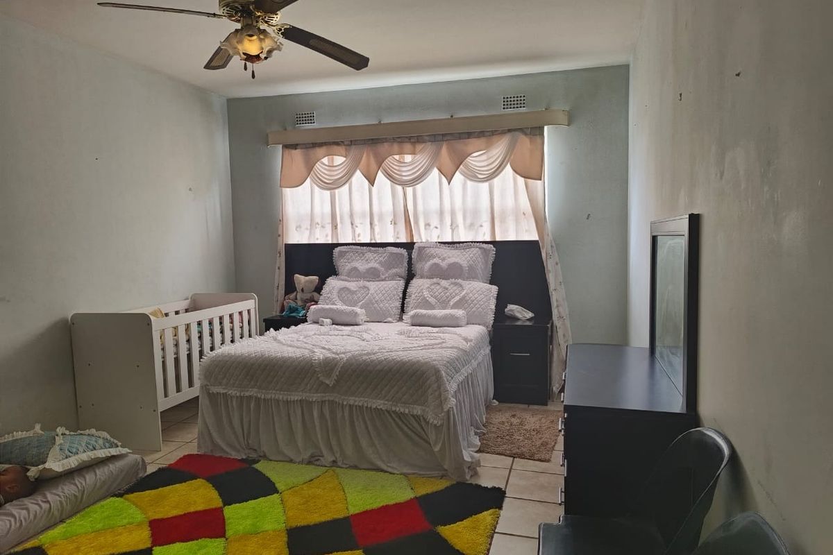A bedroom featuring tiled flooring, a ceiling fan, and built-in wall vents, providing a functional space with potential for cosmetic updates.