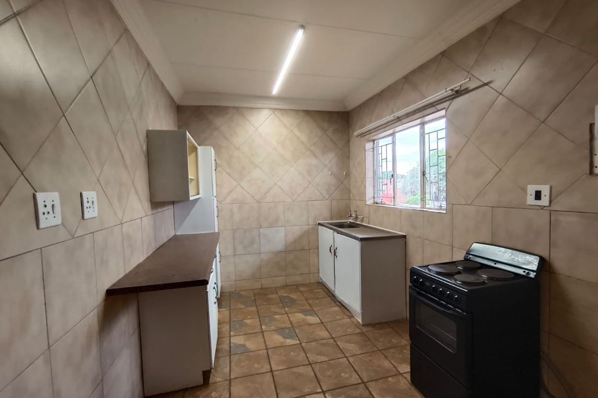 A functional kitchen featuring tiled walls and flooring, built-in cabinetry with laminate countertops, and a stainless steel sink.