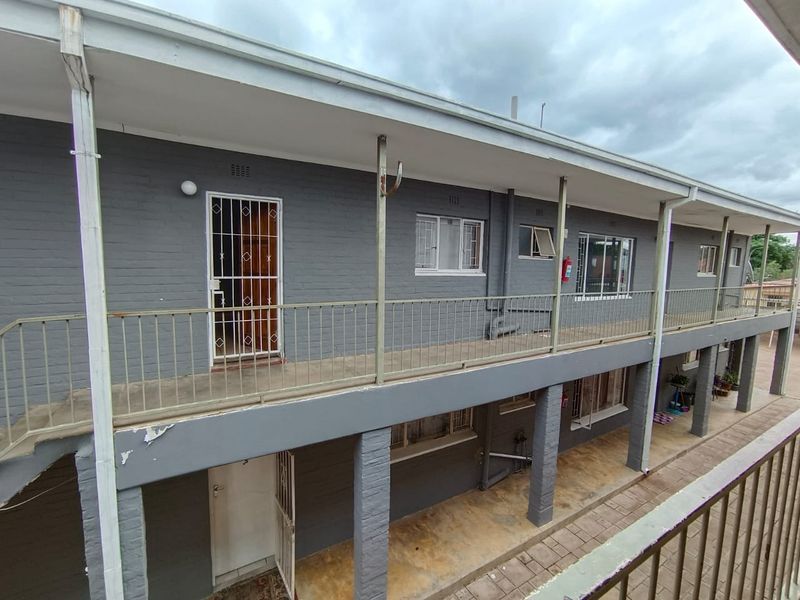 Exterior view of a multi-level apartment building featuring brick facades, metal security gates, and open-air walkways with metal railings.