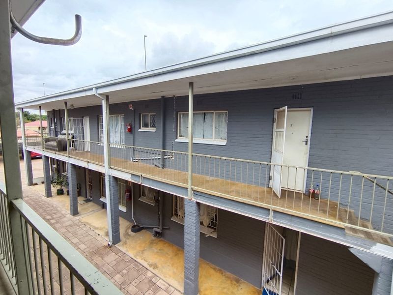 Exterior view of an apartment building featuring a covered walkway, metal balustrades, and brick facade with multiple unit entrances.