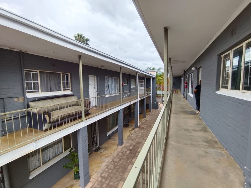 Exterior view of an apartment complex featuring a concrete walkway, metal balustrades, and painted brick facade with access to multiple units.