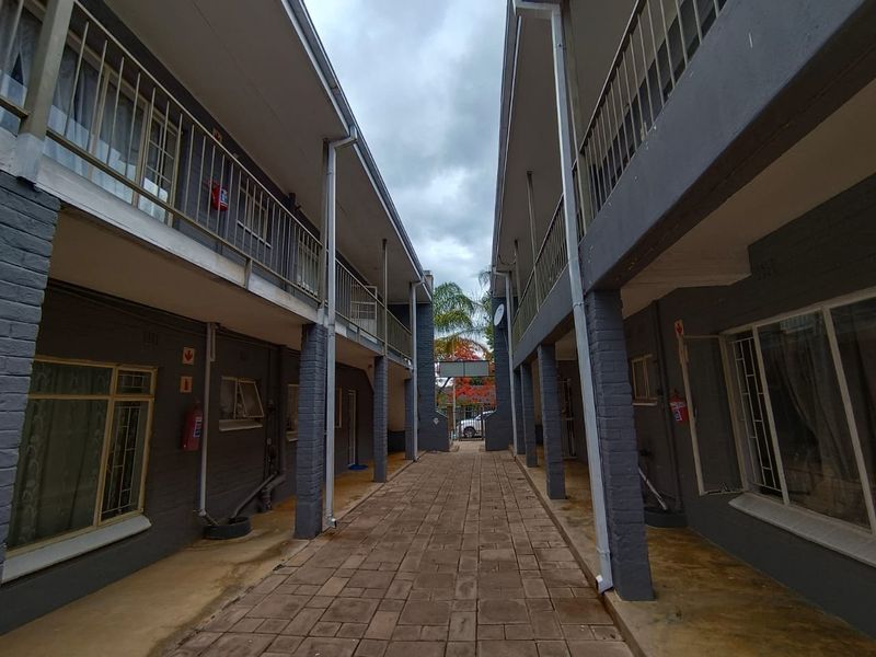 Exterior view of an apartment complex featuring a central paved walkway between two building blocks with metal balcony railings and brick support pillars.