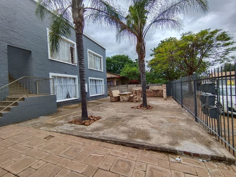 Rear exterior area featuring a brick facade, concrete paving, metal staircase, and a built-in brick braai facility within a fenced property.