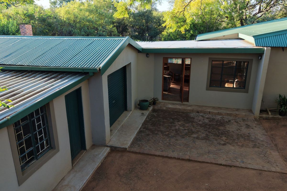 An elevated view of the rear exterior featuring a corrugated metal roof, a roller garage door, and a paved courtyard area.