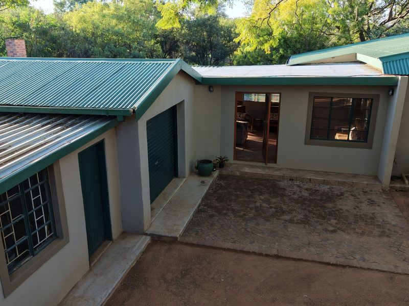 An elevated view of the rear exterior featuring a corrugated metal roof, a roller garage door, and a paved courtyard area.
