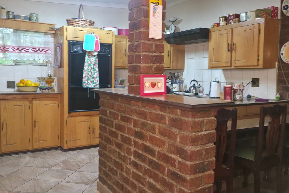 A rustic kitchen featuring wooden cabinetry, a brick breakfast bar, built-in oven, and tiled flooring, offering a traditional and functional cooking space.