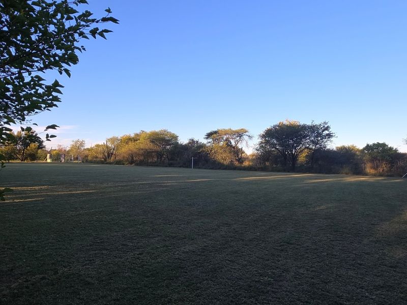 A spacious, well-maintained open lawn area surrounded by mature trees and perimeter fencing, typical of a small holding property.