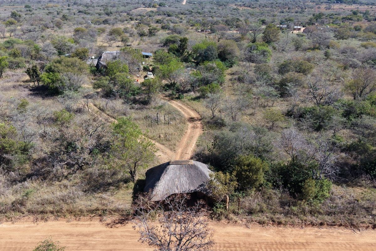 Aerial view of a small holding property featuring a thatched roof structure, dirt access roads, and surrounding natural bushveld landscape.