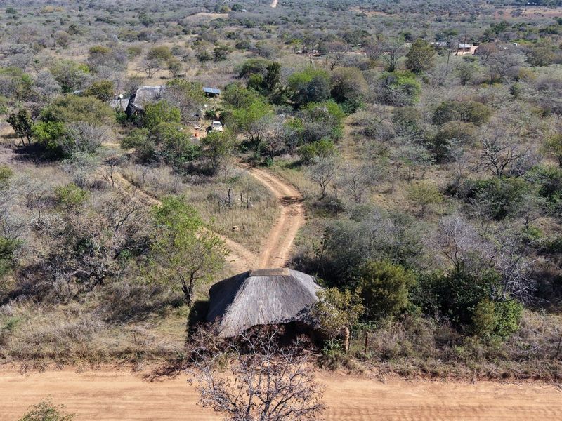 Aerial view of a small holding property featuring a thatched roof structure, dirt access roads, and surrounding natural bushveld landscape.