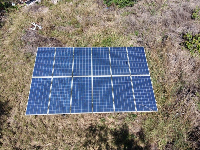 An aerial view of a ground-mounted solar panel array situated in an open field area.