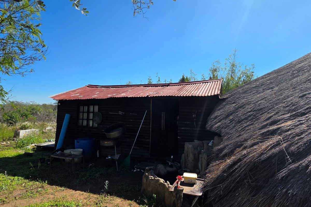 A rustic outbuilding featuring timber cladding and a corrugated iron roof, situated adjacent to a larger thatched structure on the small holding.