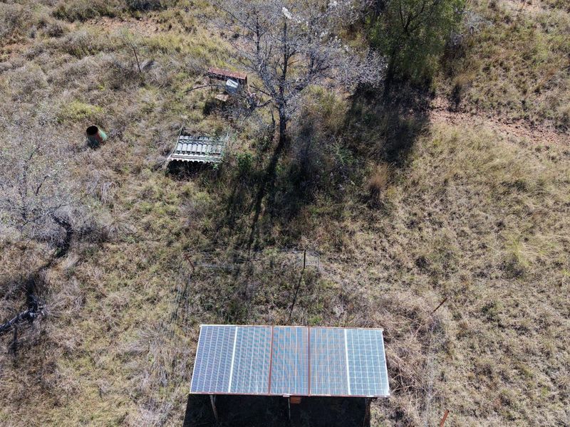 Aerial view of a small holding property featuring a ground-mounted solar panel array set within a natural, undeveloped landscape.
