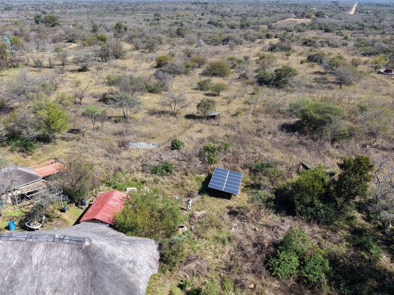 Aerial view of the small holding property featuring a thatched roof dwelling, corrugated metal roof structure, and ground-mounted solar panel array.