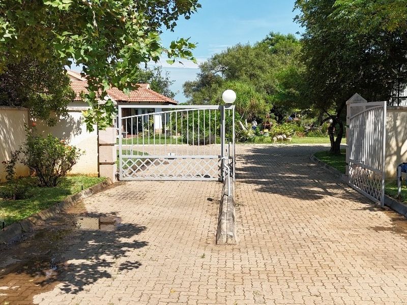A gated residential entrance featuring a paved driveway, perimeter walling, and metal security gates leading into the property grounds.
