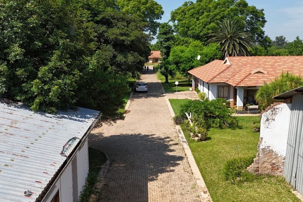 Aerial view of a residential property featuring a paved driveway, established garden, and existing structures with tiled and metal roofing.