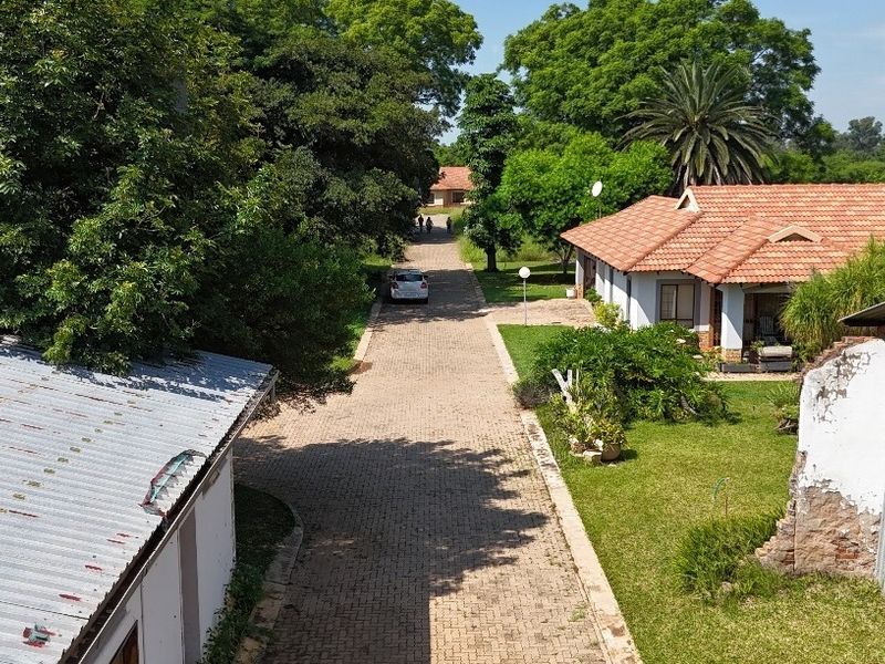 Aerial view of a residential property featuring a paved driveway, established garden, and existing structures with tiled and metal roofing.