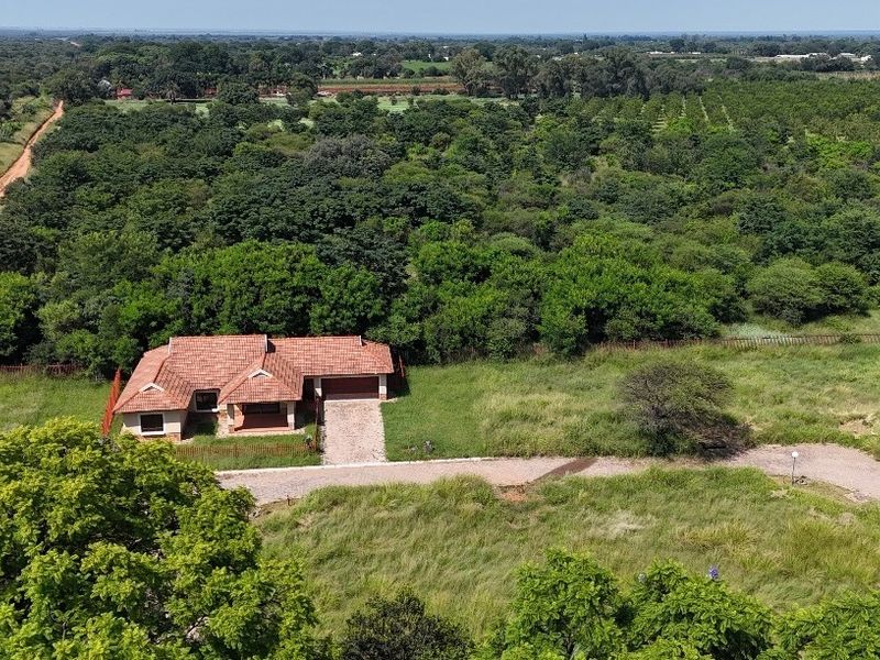 Aerial view of a residential property featuring a tiled roof home, paved driveway, and surrounding natural landscape.