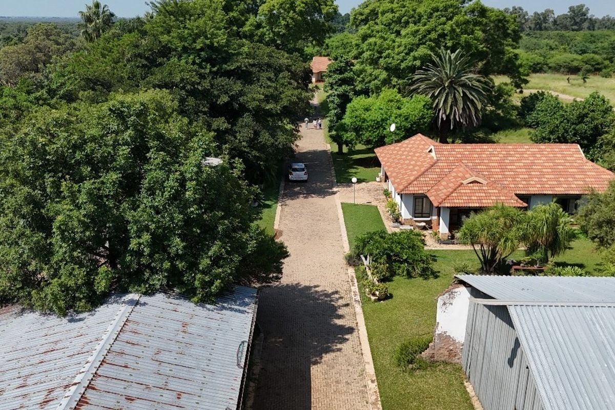 Aerial view of a residential property featuring a paved driveway, mature garden, and multiple structures with tiled and corrugated metal roofing.