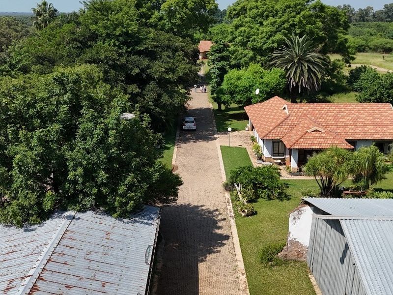 Aerial view of a residential property featuring a paved driveway, mature garden, and multiple structures with tiled and corrugated metal roofing.