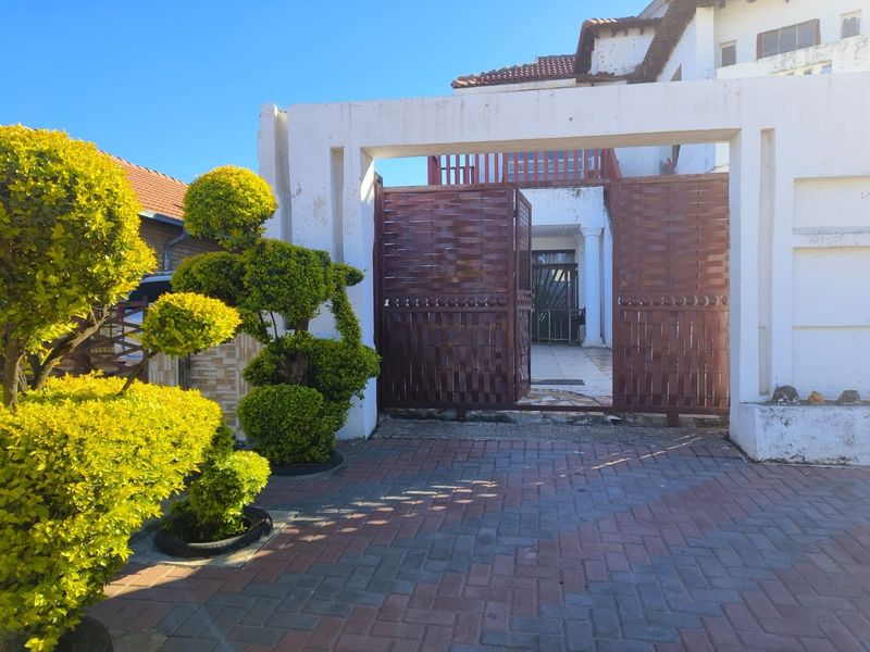 Front entrance view featuring a paved driveway, decorative topiary, and a gated entry leading to the main house structure.