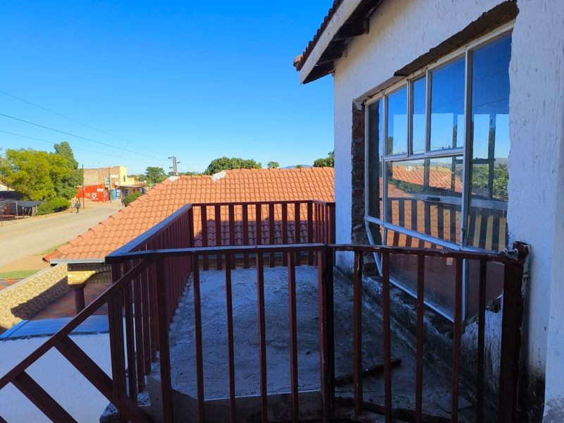 An elevated balcony area featuring a metal balustrade, requiring maintenance and finishing to the exterior wall and flooring.