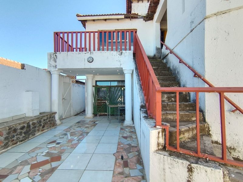 Rear exterior view featuring a tiled patio area, an external staircase leading to an upper balcony, and decorative columns.