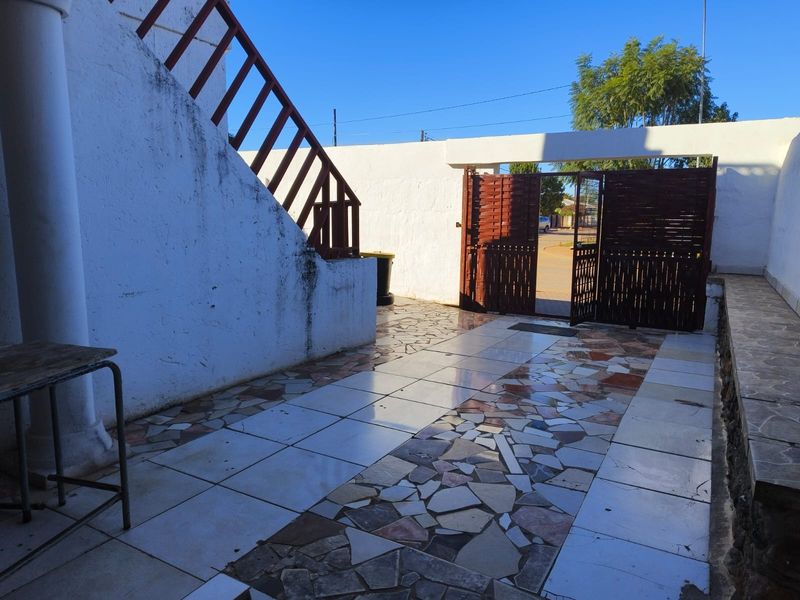 Front entrance area featuring a tiled courtyard, boundary wall with metal gate, and an external staircase leading to the upper level.