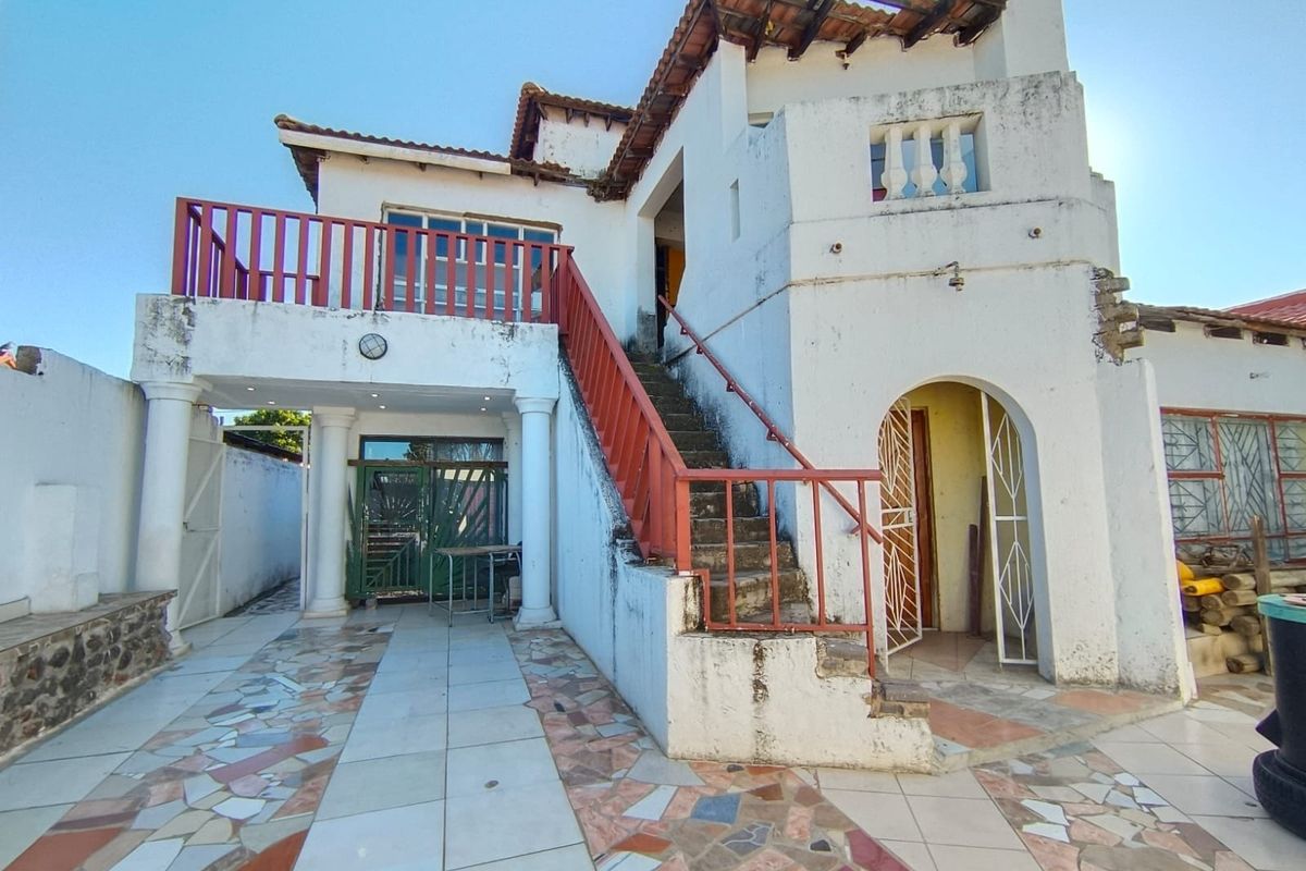 Rear exterior view of a multi-level house featuring an external staircase, balcony, and tiled patio area requiring significant maintenance and exterior refurbishment.