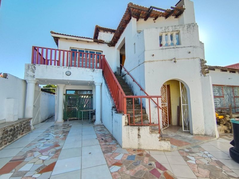 Rear exterior view of a multi-level house featuring an external staircase, balcony, and tiled patio area requiring significant maintenance and exterior refurbishment.