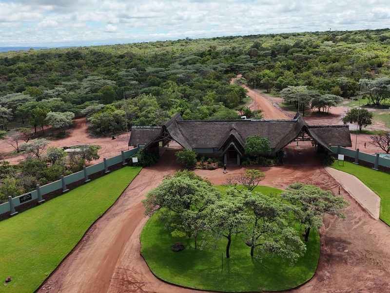 Aerial view of a gated estate entrance featuring a thatched roof building, manicured lawns, and a circular driveway set within a natural landscape.