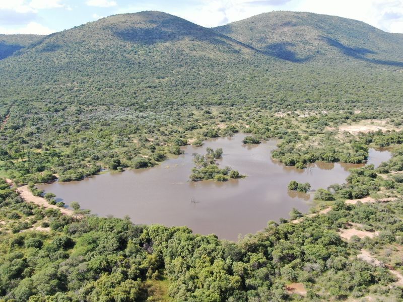 An aerial view of a large natural dam surrounded by lush indigenous bushveld and scenic mountain ranges.