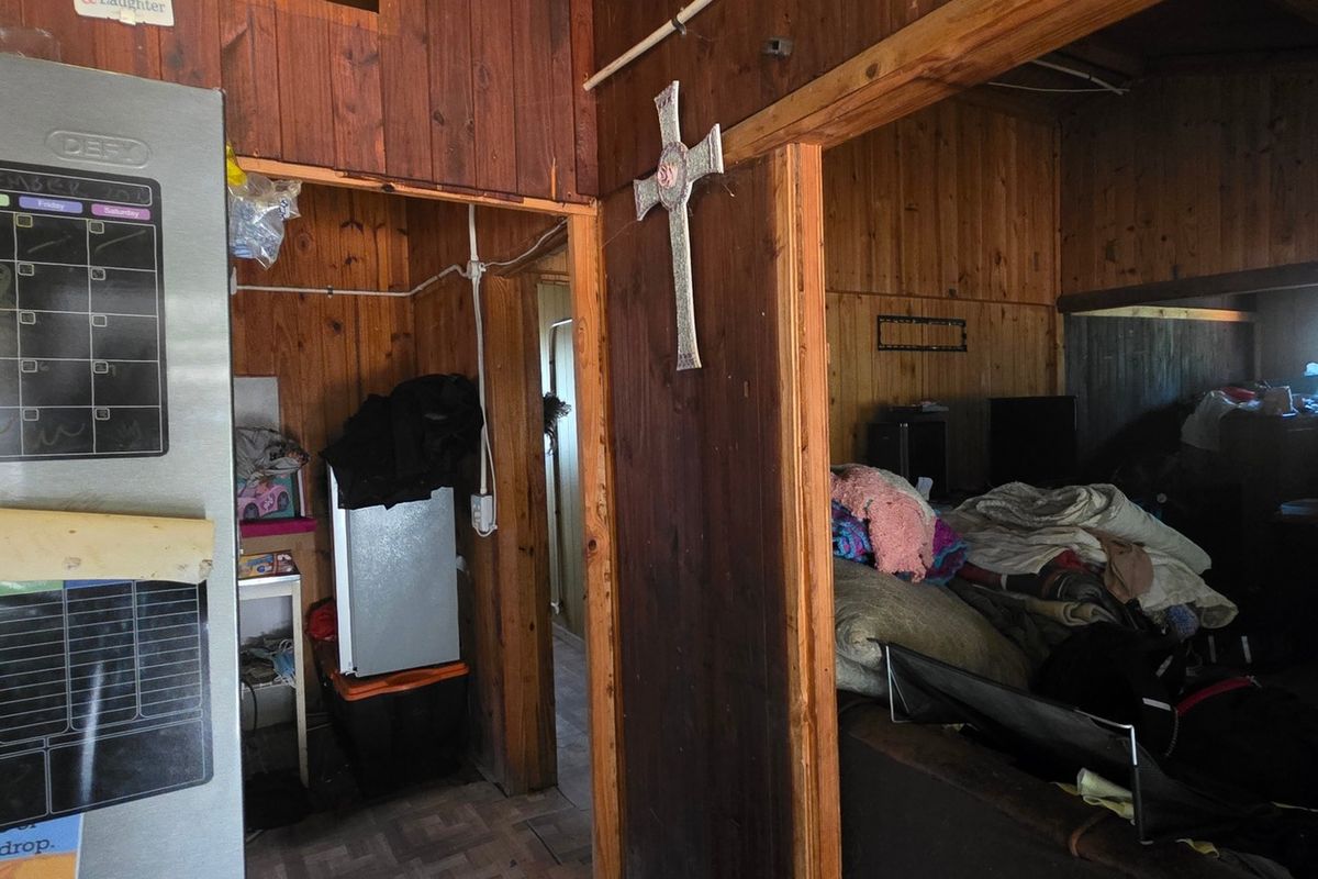 Interior view of a rustic living area featuring extensive timber wall paneling and exposed structural beams, showing signs of age and wear.