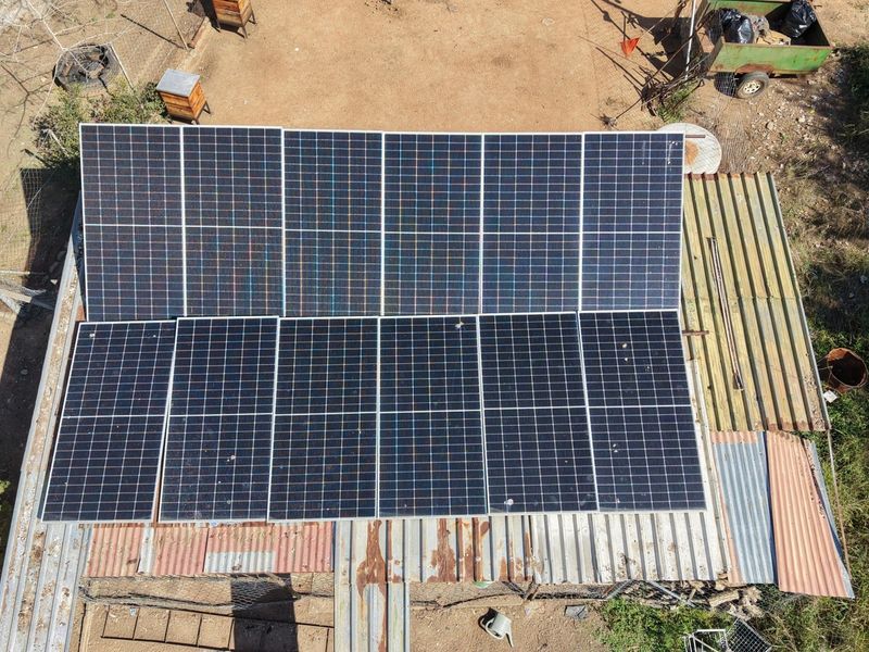 Aerial view of a solar panel array installed on a corrugated metal roof showing signs of surface corrosion and weathering.