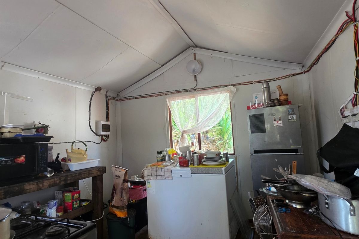 A rustic kitchen area featuring exposed electrical wiring, a vaulted ceiling, and basic utility surfaces in a functional farm-style setting.