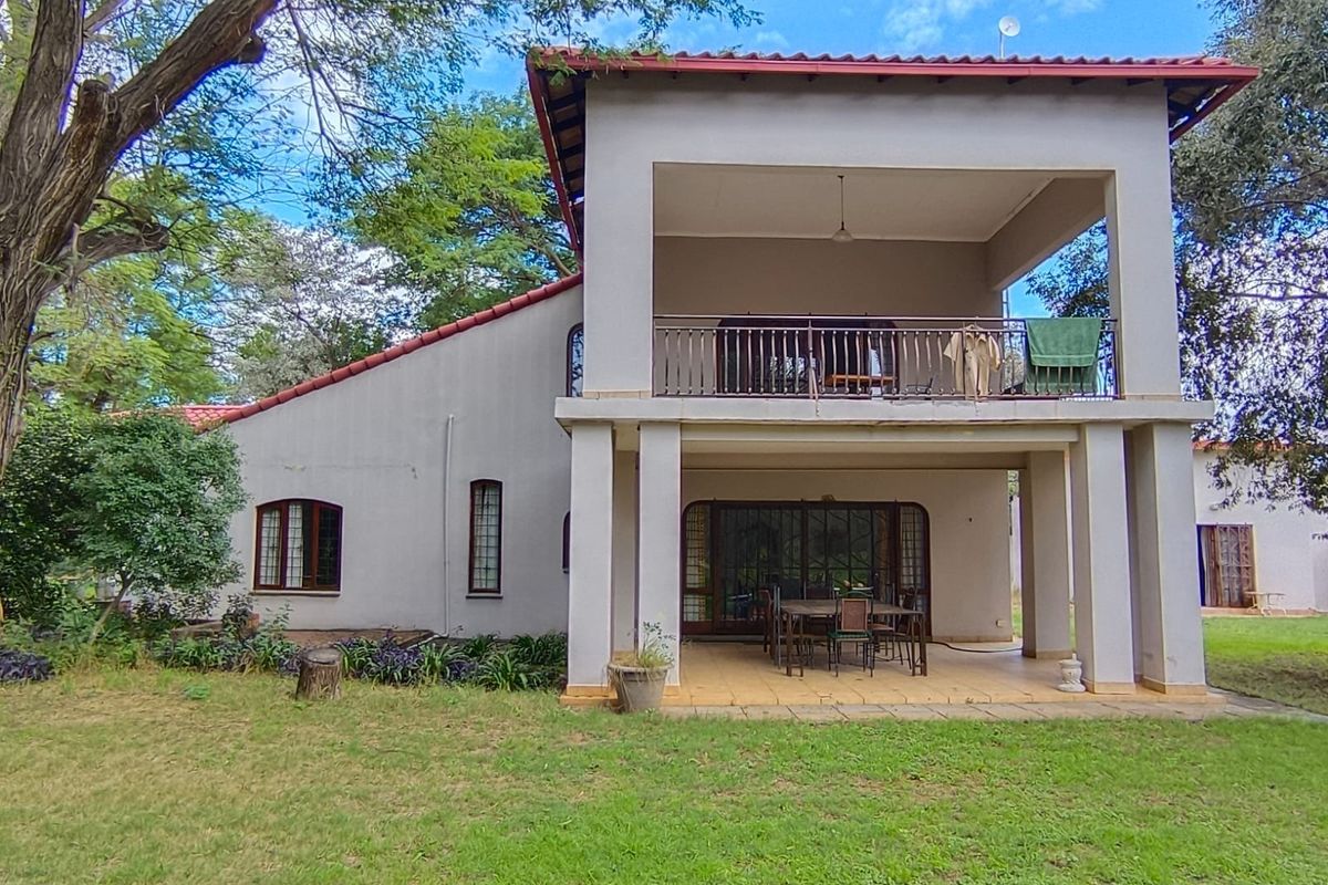Rear view of a two-story farm house featuring a covered ground-floor patio, an upper-level balcony with metal railing, and a spacious garden area.