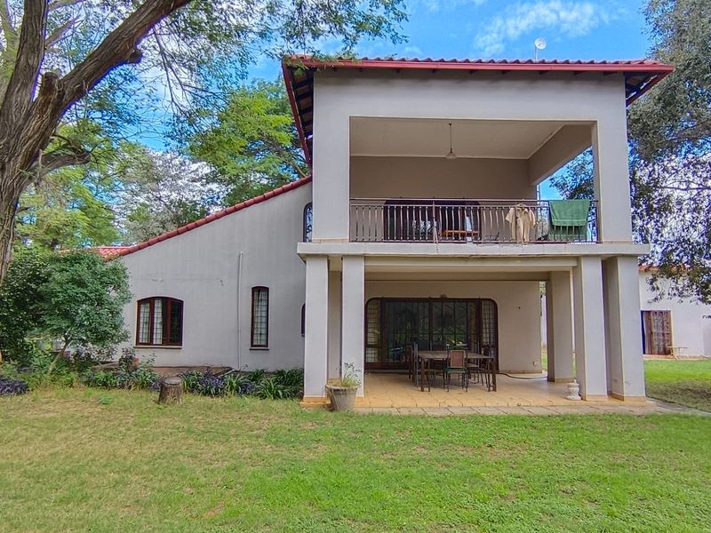 Rear view of a two-story farm house featuring a covered ground-floor patio, an upper-level balcony with metal railing, and a spacious garden area.