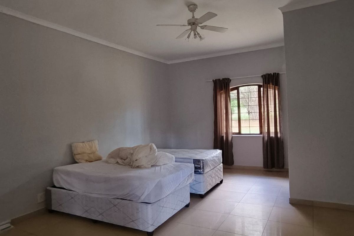 A spacious bedroom featuring neutral walls, tiled flooring, a ceiling fan, and an arched window providing natural light.