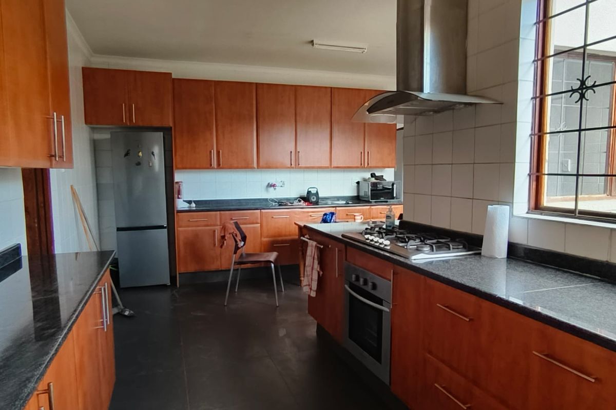 A functional kitchen featuring wooden cabinetry, granite countertops, a gas hob, built-in oven, and a stainless steel extractor fan.