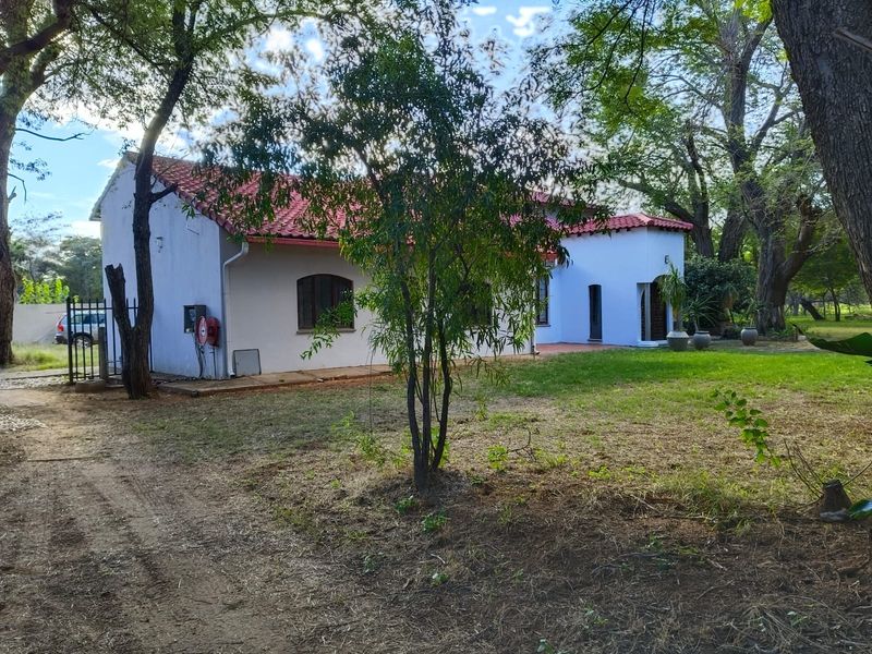 Rear view of a farm-style residence featuring white exterior walls, terracotta roof tiles, and arched windows set within a spacious garden area.