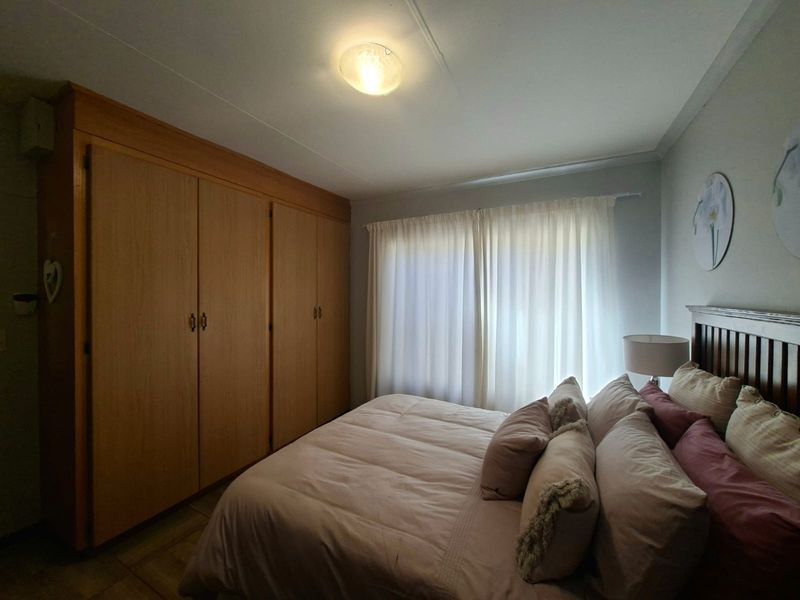 A bedroom featuring built-in wooden cupboards and a window with sheer curtains, providing a functional and comfortable living space.
