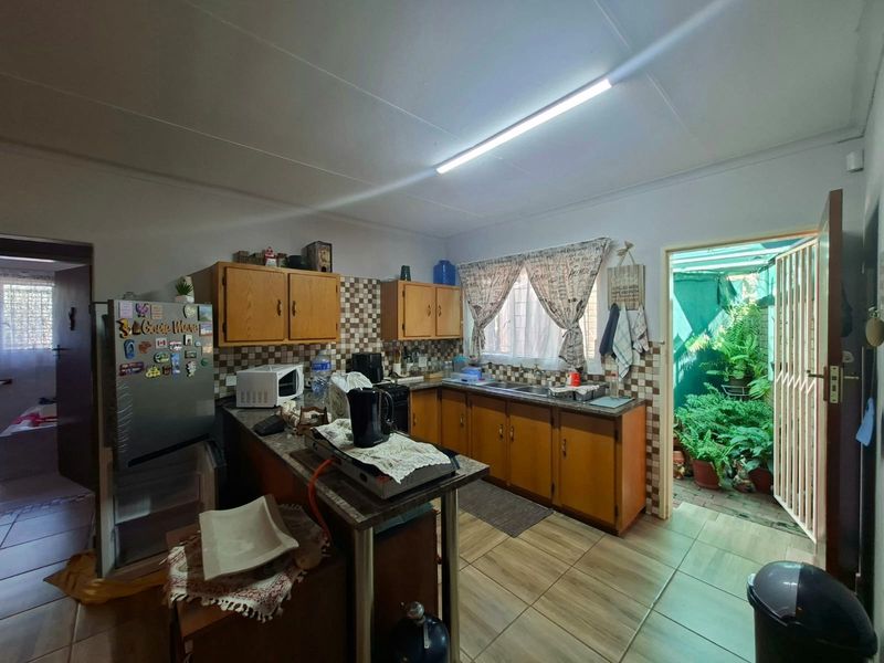 A functional kitchen featuring wooden cabinetry, tiled backsplash, and direct access to an outdoor area through a security gate.
